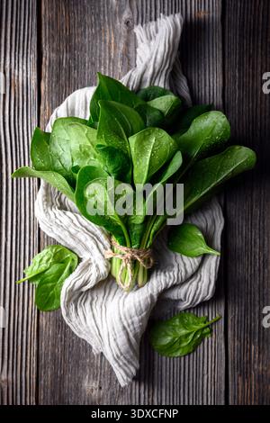 Flache Lage gewaschener Spinatstränge, mit Garn auf Baumwollküchentuch gewickelt. Gartenarbeit, sauberes Gemüse und umweltfreundliches Lifestyle-Konzept Stockfoto