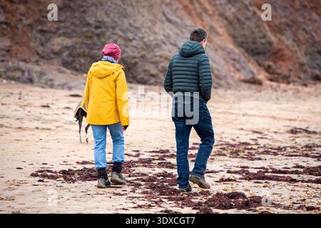 Mann und Frau mittleren Alters Paar Wanderhund am Sandstrand am Meer in der Wintersaison in warmer Winterkleidung. Stockfoto