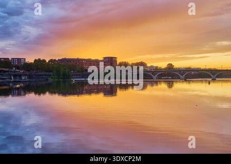 Lebendiger Sonnenuntergang über dem Fluss Garonne und der Pont des Catalans in Toulouse, Frankreich, mit farbenfrohen Himmelsreflexen im Wasser. Stockfoto