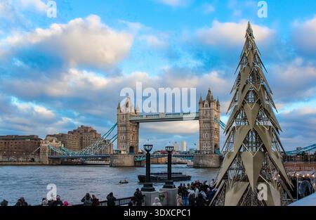 London, Großbritannien - 25. Dezember 2025: Die ikonische Tower Bridge steht im Hintergrund und der geometrische Weihnachtsbaum schimmert auf dem Markt. Stockfoto