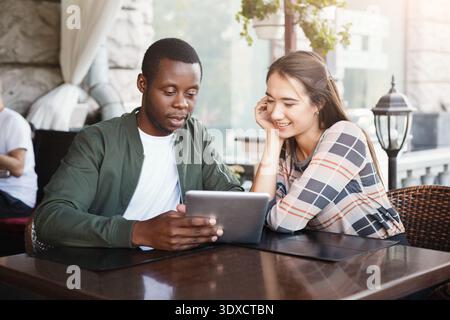 Zwei Personen, die ein Tablet anschauen, während sie an einem Cafe-Tisch in der Nachmittagssonne sitzen Stockfoto