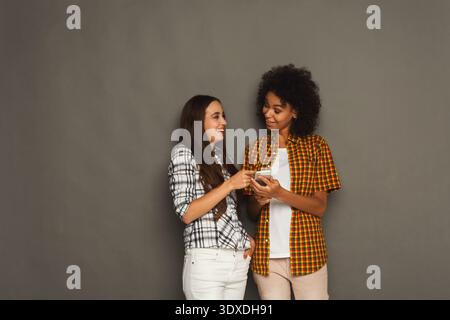 Zwei Freunde sehen sich ein Telefon an, während sie vor grauem Hintergrund stehen Stockfoto