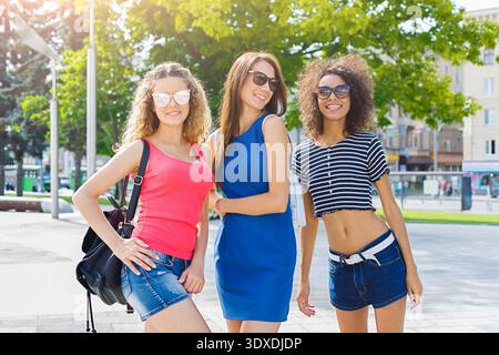 Drei Freunde posieren zusammen in einer sonnigen Outdoor-Umgebung mit urbanem Hintergrund und Grün Stockfoto