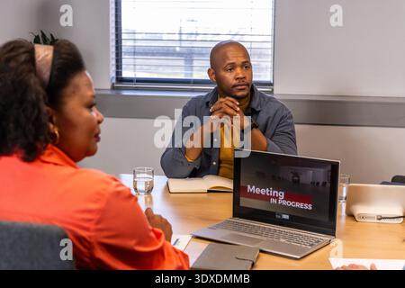 Afroamerikanisches Team, das am Konferenztisch sitzt und die Besprechung mit einem Laptop ansieht Stockfoto
