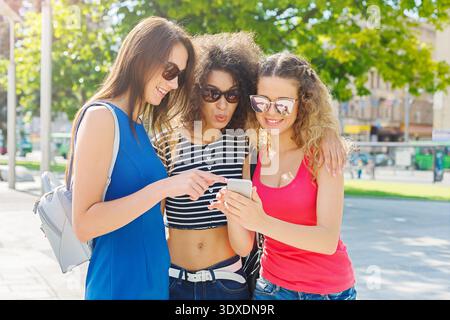 Drei Freunde genießen einen sonnigen Tag im Park, während sie gemeinsam ein Smartphone ansehen Stockfoto
