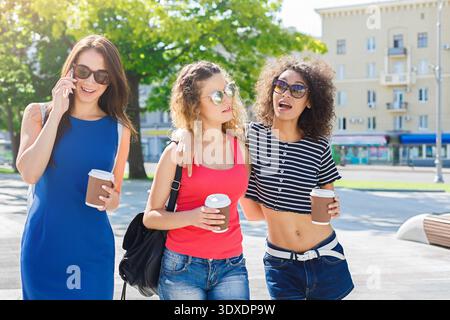 Drei Freunde spazieren zusammen und genießen an einem sonnigen Tag Kaffee in einer Stadt Stockfoto