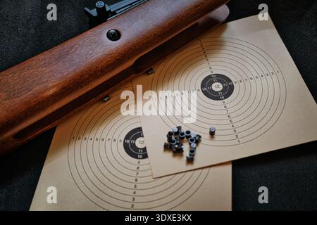 Nahaufnahme eines modernen Gewehrauslösers mit einrastendem Sicherheitstaste, positioniert über einem Papierschießziel für präzises Training. Stockfoto