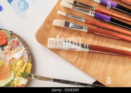 Ölmalpalette mit Pinsel und Palettenmesser auf leerer Leinwand im Künstleratelier-Arbeitsbereich Stockfoto