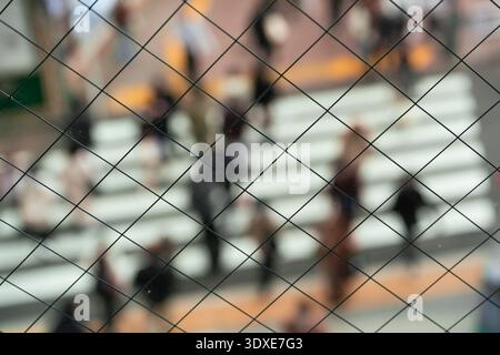 Maschendrahtzaun mit unscharfen Menschen, die die Straße in Shibuya, Japan, überqueren Stockfoto