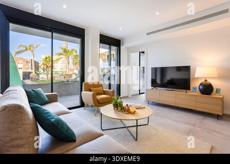 Modernes Wohnzimmer mit großen Glastüren, hölzerner Medienkonsole, gemütlichen Sitzgelegenheiten und viel Tageslicht schaffen ein elegantes und einladendes atmos Stockfoto