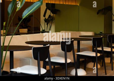 Ein modernes Café mit eleganten schwarzen Tischen und Stühlen, ergänzt durch weiche beige Sitzbänke, schafft eine stilvolle Atmosphäre Stockfoto