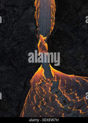 Aus der Vogelperspektive glühende Lava, die sich durch die dunkle, zerklüftete Landschaft schlängelt, starker Kontrast zwischen feurigem Orange und Anthrazit, Grindavik, Island. Stockfoto