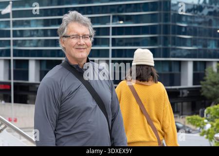 Ein älterer Mann, der neben einem Geländer auf Betontreppen auf der plaza stand, trug eine graue Jacke und Brille Stockfoto