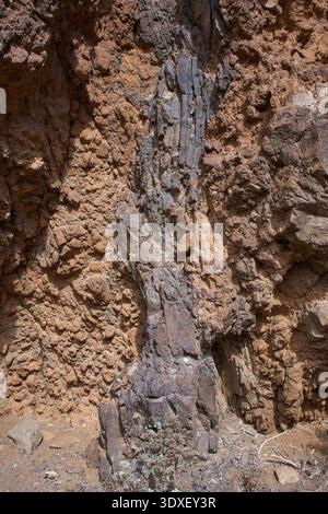Nahaufnahme der dramatisch gestuften roten und ockerfarbenen vulkanischen Klippen mit kontrastierenden Basaltfelsen-Texturen und spärlicher endemischer Vegetation in der Anaga Re Stockfoto