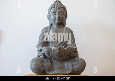 Bronzestatuette, die Buddha auf einer kleinen hölzernen Plattform darstellt. Die Statuette ist vor hellem Hintergrund fotografiert Stockfoto