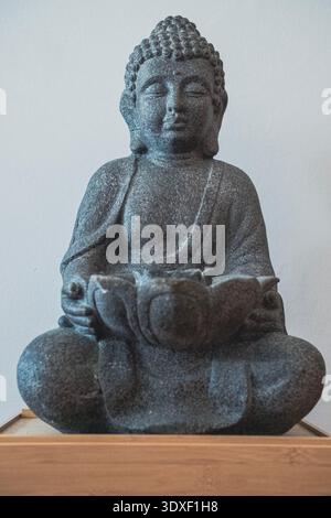 Bronzestatuette, die Buddha auf einer kleinen hölzernen Plattform darstellt. Die Statuette ist vor hellem Hintergrund fotografiert Stockfoto