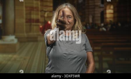 Ältere blonde Frau zeigt mit gestreckter Hand und ruhigem Ausdruck im historischen Gebäude den Finger auf die Kamera; Selbstvertrauen ist eine Herausforderung. Stockfoto