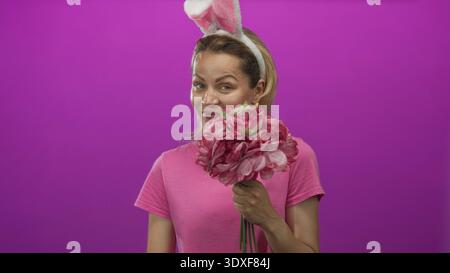Frau mit Haarband mit Hasenohren hält einen leuchtenden Blumenstrauß und zeigt den Finger im Studio nach oben; Freude feiern. Stockfoto