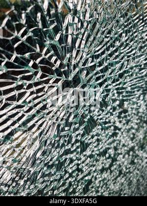 Hintergrund mit zersplittertem Glasmuster. Nahaufnahme eines zersplitterten Sicherheitsglases mit radialem Schlagmuster. Das Netz der Frakturen erzeugt eine dramatische Textur. Stockfoto