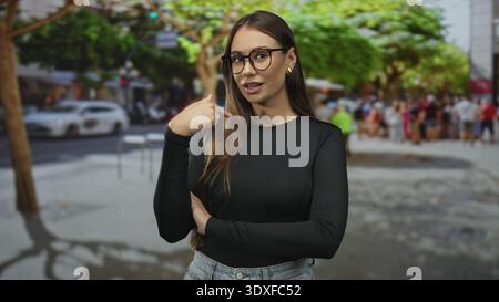 Junge Frau zeigt den Zeigefinger nach oben auf die Straße, Arme gefaltet, Brille und Jeans getragen; Vertrauensunterweisung. Stockfoto