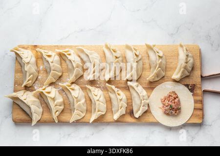 Rohe japanische Gyoza-Knödel mit Fleisch und Pilzen auf hölzernem Schneidebrett, weißer Marmorhintergrund, Blick von oben Stockfoto
