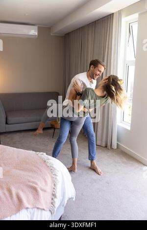 Im modernen Schlaf- und Wohnbereich mit Kingsize-Bett und Sofa tanzen Sie spielerisch am Fenster. Lifestyle, Intimität, Entspannung, Harmonie, gemütlich, modern, Wohnkultur || Modell veröffentlicht Stockfoto