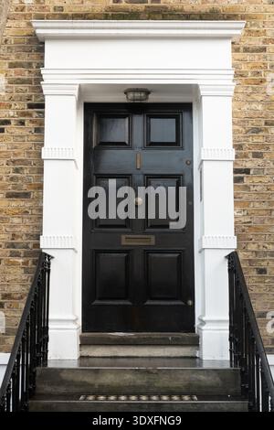 Klassische schwarze Vordertür mit weißem Rahmen auf Ziegelsteingebäude in London Stockfoto