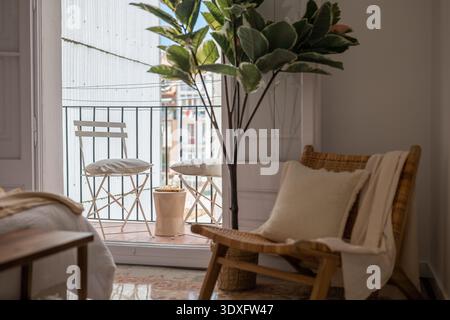 Gemütliche Inneneinrichtung mit Holzstuhl, Topfpflanze und Balkon. Tageslicht beleuchtet den Raum und schafft eine warme Atmosphäre. Stockfoto