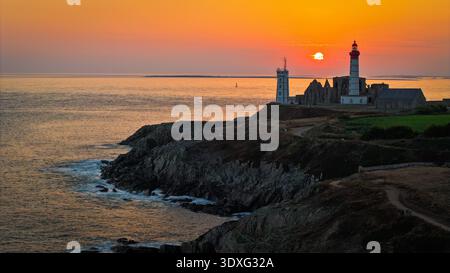Aus der Vogelperspektive von Phare de Saint-Mathieu, hoch vor dem feurigen Sonnenuntergang, während Wellen gegen die zerklüftete Küste, Plougonvelin, Bretagne, Fra, krachen Stockfoto