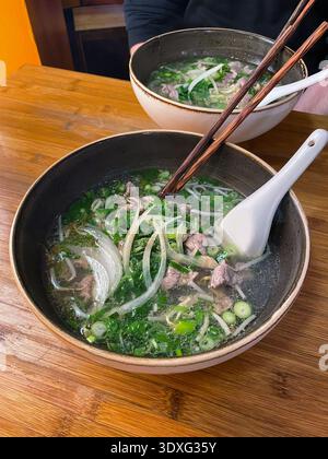 Traditionelle vietnamesische Pho Bo Rindfleischnudelsuppe in einer Keramikschale mit Reisnudeln, Rindfleisch in Scheiben, frischen Kräutern und grünen Zwiebeln. Stockfoto