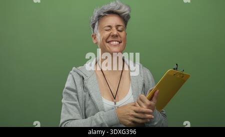 Kaukasische Frau mit kurzen Haaren, grauem Hoodie und gelbem Klemmbrett, während sie im Studio lächelt; Zuversicht. Stockfoto