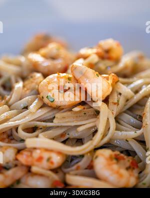 Nahaufnahme von Linguine-Pasta mit gekochten Garnelen und Kräutern, serviert auf einem weißen Teller. Das Bild wird in vertikaler Ausrichtung fotografiert. Stockfoto