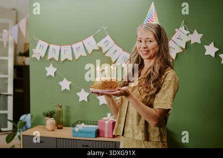 Porträt einer kaukasischen Frau mittleren Alters, die lächelt, während sie Geburtstagskuchen hält Stockfoto