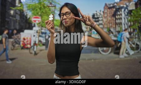 Thailändische Frau hält ein weißes Puzzleteil und blitzt mit der rechten Hand auf eine Straße, die von Fahrrädern und Backsteinhäusern gesäumt ist; Neugier entdeckt. Stockfoto