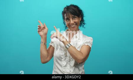 Die ranghanische Frau zeigt mit den Zeigefingern, während sie lächelt, trägt silberne Armbänder und weiße Bluse im Studio; fröhliche Wärme. Stockfoto