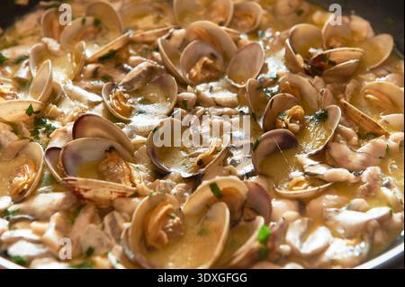 Frische Venusmuscheln in einer Pfanne, angereichert mit einem reichhaltigen Weißwein und Knoblauchsoße, garniert mit frischer Petersilie Stockfoto
