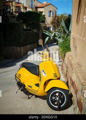 San-Tropez, Frankreich-Feb 21,2026: Gelber italienischer Roller parkt in der Nähe des Hauses mit gelber Mauer an der Straße von San-Tropez Stockfoto
