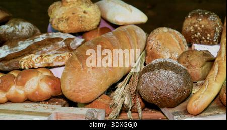 Frisch gebackenes Brot wird tagsüber auf einem Holztisch in einer Bäckerei ausgestellt und verschiedene Brotsorten sichtbar Stockfoto