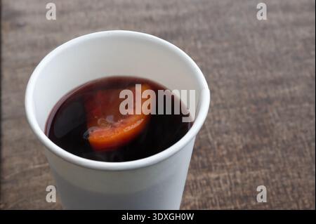 Heißer gewürzter Wein mit Orangenscheibe ruht auf Holztisch in winterlicher Marktatmosphäre Stockfoto