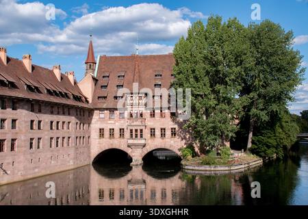 Das Krankenhaus Heilig Geist befindet sich an der Pegnitz in der Nürnberger Altstadt und bietet mittelalterliche Architektur mit roten Ziegeldächern und Bogenfenstern. Stockfoto