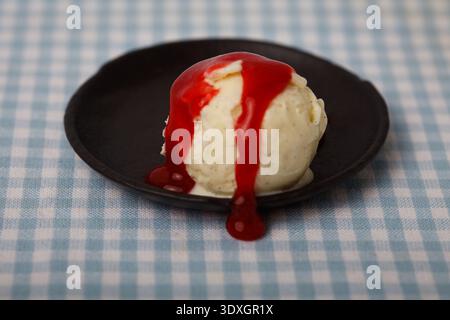 Ein einziger Messlöffel Premium-Vanilleeis mit dicker, glänzender Erdbeersauce Stockfoto