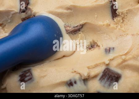 Ein Hochwinkel-Makrofoto eines blauen Eisschaufels, der durch eine dichte Portion Erdnussbutter-Eis fährt Stockfoto