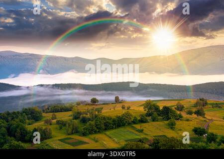 Sonnenuntergang über bergigen ländlichen Gebieten im Frühling. Abgelegene Berglandschaft mit waldreichen Hügeln. Wunderbarer nebeliger Ort der alpinen Landsi Stockfoto