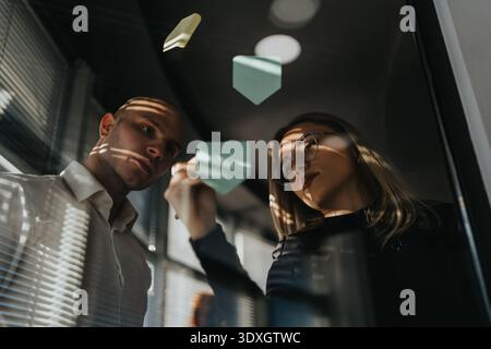Zwei Kollegen bewerten Haftnotizen auf einer Glastafel in einem modernen Geschäftsumfeld Stockfoto