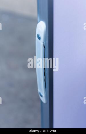 Eine minimalistische Nahaufnahme eines weißen Kunststoffgriffs an einer Tür. Die Komposition verfügt über eine geringe Schärfentiefe mit kühlem Blau, Grau und Lavendelt Stockfoto