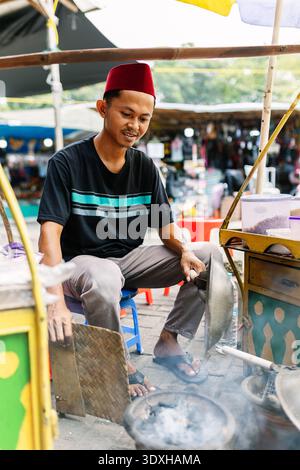 Indonesischer Straßenverkäufer, der lokale Gerichte auf einem traditionellen Markt zubereitet Stockfoto