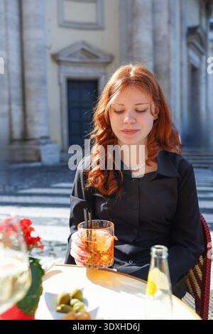 Frau, die sich bei einem Drink auf der gemütlichen Terrasse in Rom entspannt. Tourismus, Mode und mediterrane Stadtatmosphäre. Stockfoto