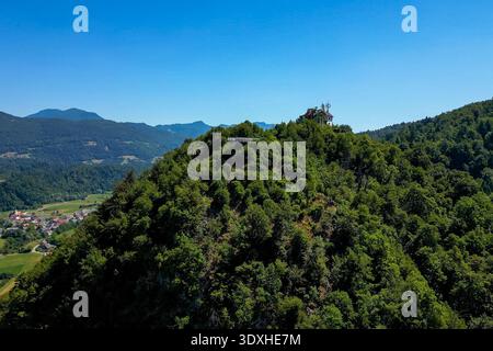 Blick aus der Vogelperspektive auf den üppigen, baumbedeckten Hügel Stari Grad (altes Schloss) in Kamnik, Slowenien, mit moderner Aussichtsplattform und Berghütte Stockfoto