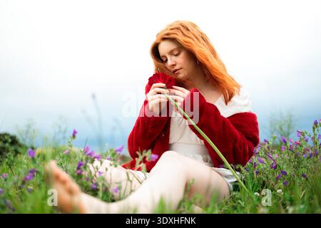 Eine junge Frau im roten Pullover, die in der Wildflower Meadow sitzt Stockfoto