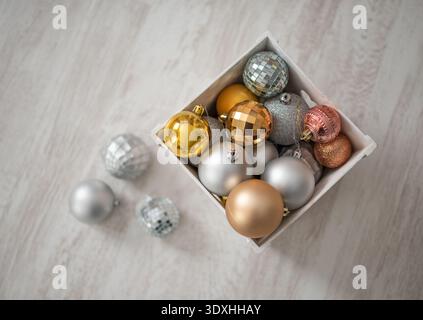 Festliche Komposition mit goldenen silbernen und rosafarbenen Weihnachtskugeln in Kiste auf hellem Holzboden, die sich auf Neujahr vorbereiten. Stockfoto
